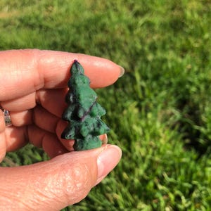 May include: A small green and purple carved gemstone tree figurine. The tree is carved in the shape of a Christmas tree and has a detailed design.