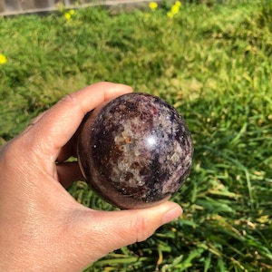 May include: A polished purple and black sphere of amethyst crystal. The sphere is smooth and has a high gloss finish.