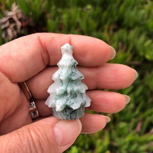 May include: A small, green and white agate tree carving. The tree is carved in a traditional Christmas tree shape.