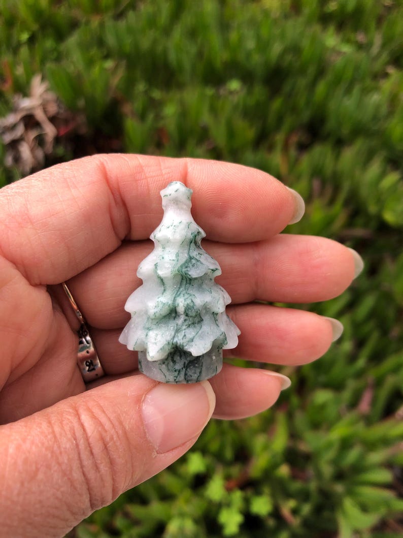 May include: A small, green and white agate tree carving. The tree is carved in a traditional Christmas tree shape.