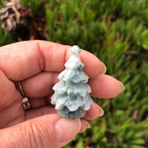 May include: A small, carved green and white agate tree ornament. The tree is about 2 inches tall and has a detailed, realistic design.