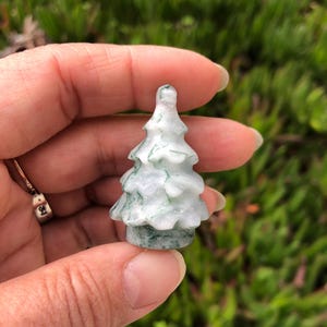 May include: A small, carved green and white jade tree ornament. The tree is about 2 inches tall and has a detailed, realistic design.