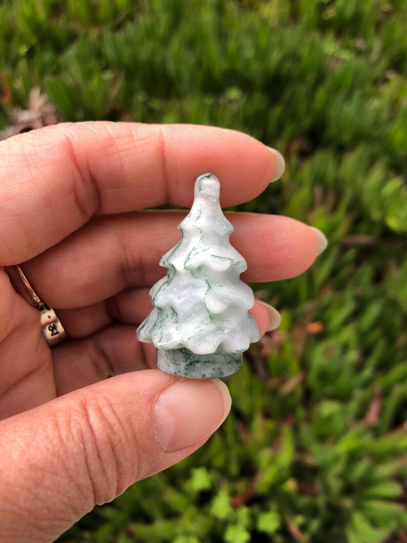 May include: A small, carved green and white jade tree ornament. The tree is about 2 inches tall and has a detailed, realistic design.
