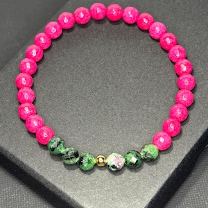 May include: A beaded bracelet featuring a continuous loop of faceted hot pink beads, accented by a small section of green and black speckled zoisite beads and a single smooth, polished gold-tone metal bead centered among the green stones.