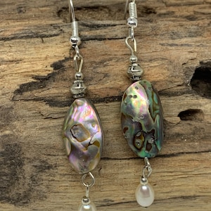 May include: A pair of silver dangle earrings with iridescent abalone shell oval beads and white pearl accents.