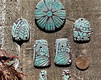 Könnte beinhalten: Ein Set aus sieben Keramikfliesen in einem Teal- und Braunton. Die Fliesen zeigen verschiedene geometrische und florale Muster.
