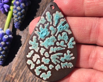 May include: A teardrop-shaped pendant with a brown background and a turquoise and white abstract pattern.