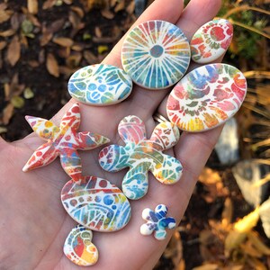 May include: A collection of colorful ceramic tiles with various patterns, including a starfish, a flower, and a circle. The tiles are hand-painted with intricate details and vibrant colors.