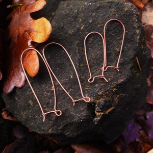 May include: Three pairs of copper wire earring hooks, lying on a dark gray rock surface.