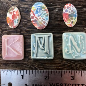 May include: Three ceramic tiles with the letters K, M, and N in a decorative font.  Three oval ceramic tiles with colorful abstract designs.