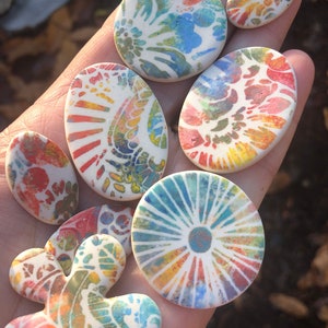 May include: A collection of seven ceramic tiles with colorful, abstract patterns. The tiles are various shapes and sizes, including round, oval, and a flower shape. The colors are bright and vibrant, including shades of blue, green, yellow, orange, and red.