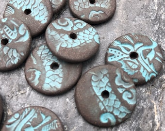 May include: A collection of brown ceramic buttons with a blue and white fish design. The buttons have a hole in the centre for sewing.