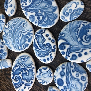 May include: A selection of white ceramic pieces with blue floral patterns. The pieces are in various shapes, such as ovals, circles, and rectangles. The blue designs feature intricate leaf and swirl motifs, creating a decorative aesthetic.