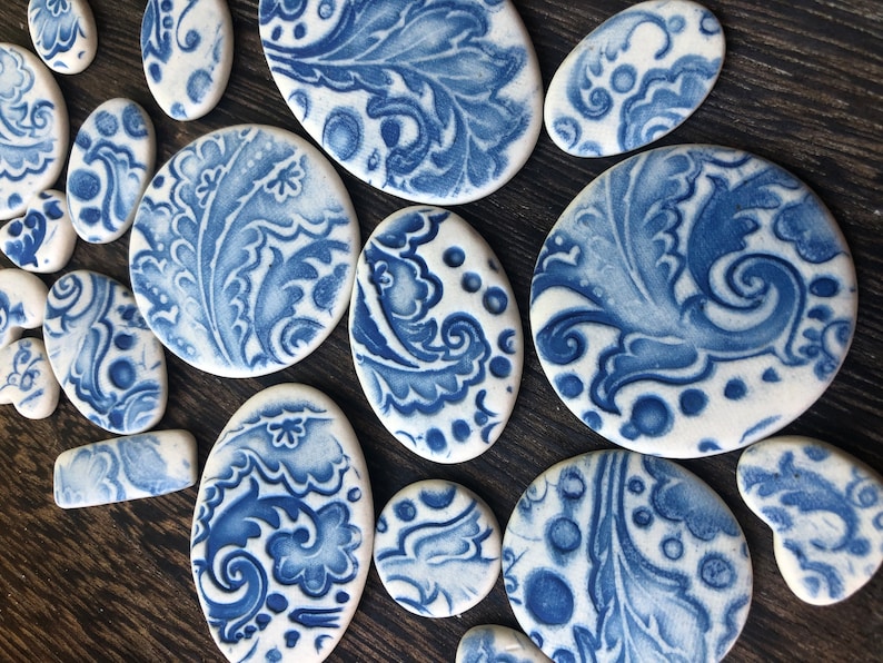 May include: A selection of white ceramic pieces with blue floral patterns. The pieces are in various shapes, such as ovals, circles, and rectangles. The blue designs feature intricate leaf and swirl motifs, creating a decorative aesthetic.