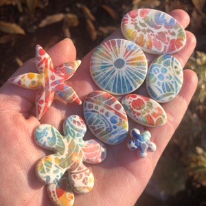 May include: A collection of colorful ceramic tiles with various patterns, including a star, a flower, and a circle. The tiles are hand-painted with intricate designs and vibrant colors.