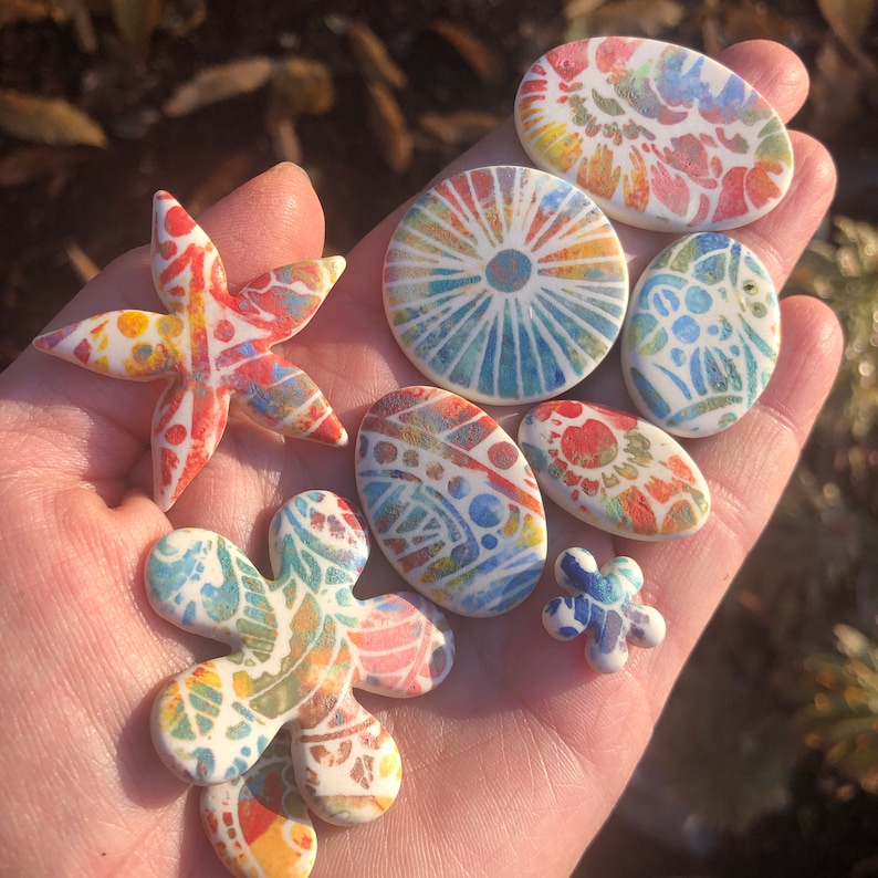 May include: A collection of colorful ceramic tiles with various patterns, including a star, a flower, and a circle. The tiles are hand-painted with intricate designs and vibrant colors.