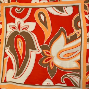 Peut inclure: Un foulard en soie à motif paisley rouge, blanc et orange avec une bordure marron. Le foulard porte la signature "Cacharel" en bas à droite.