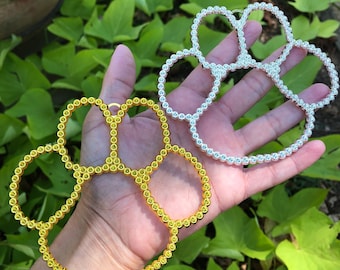 May include: Two paw-shaped jewelry pieces made of small beads. One is gold and the other is silver.