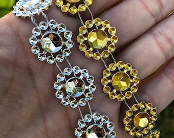 May include: A silver and gold beaded chain with alternating round rhinestones. The chain is made of a thin, clear string and features a repeating pattern of silver and gold rhinestones.