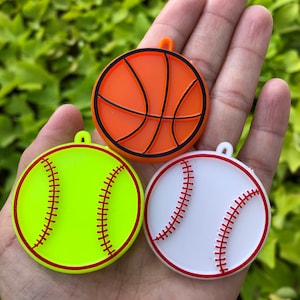 May include: Three colorful keychains shaped like sports balls: a yellow and red baseball, a white and red baseball, and an orange basketball.