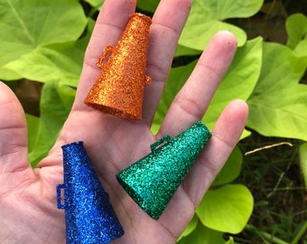 May include: Three mini foam megaphones with glitter. One is orange, one is blue, and one is green.