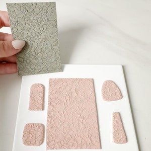 May include: A set of five pink polymer clay shapes with a floral embossed pattern. The shapes include a rectangle, a rounded rectangle, a teardrop, a rounded square, and a long rectangle. The shapes are arranged on a white surface.