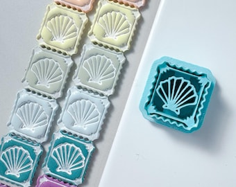 Pode incluir: Uma coleção de cortadores de biscoitos quadrados com um design de concha, dispostos em duas filas verticais com uma variedade de cores pastel e vibrantes, incluindo rosa, amarelo, verde, azul e roxo, ao lado de um cortador azul brilhante.
