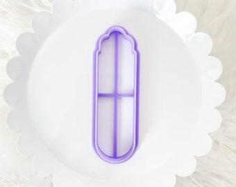 May include: A purple plastic cookie cutter shaped like a tall, narrow window with a rounded top and a cross-shaped design inside.