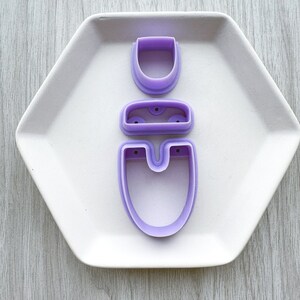 May include: A set of three purple plastic cookie cutters shaped like a snowman. The cutters are stacked on top of each other, with the largest cutter at the bottom and the smallest cutter at the top.