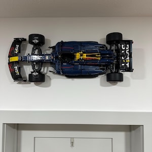 Könnte beinhalten: Ein blaues und schwarzes Lego Formel-1-Rennwagen mit Red Bull Branding und dem Text "Red Bull" und "Bybit" an der Seite. Das Auto ist an einer weißen Wand montiert.