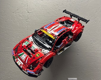 May include: A red, white, and blue Lego Ferrari 488 GTE race car with the number 51 on the side. The car is mounted on a wall and has a black spoiler.