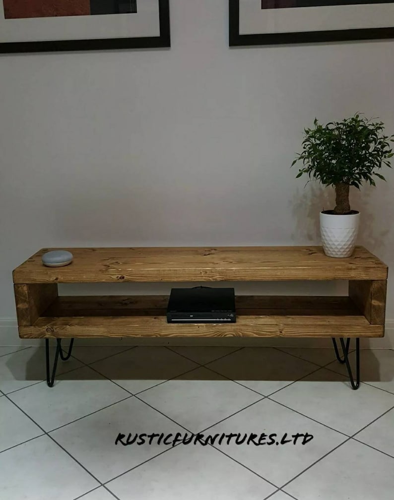 May include: A rustic wooden TV stand with a shelf and hairpin legs. The stand is made of reclaimed wood and has a natural finish. The stand is 47 inches wide, 16 inches deep, and 18 inches tall.