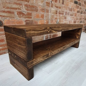 May include: A dark brown wooden bench with a shelf underneath. The bench is made of reclaimed wood and has a rustic finish.