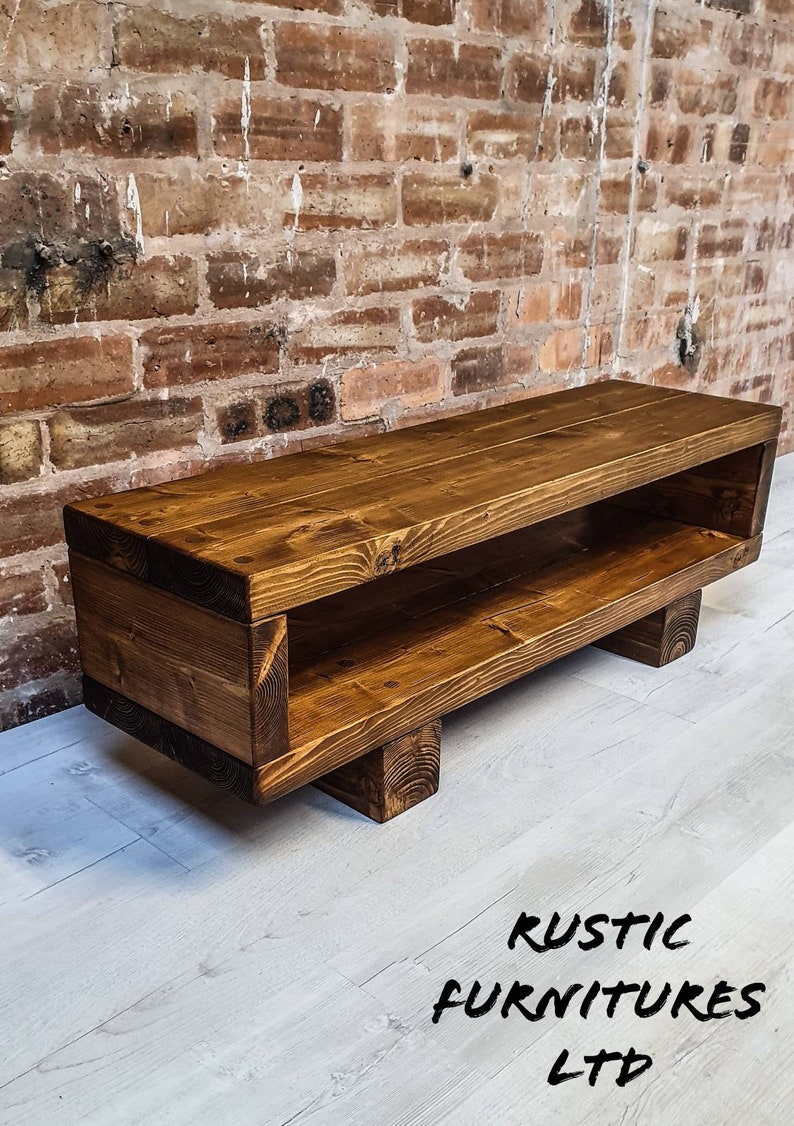 May include: A rustic wooden TV stand with a shelf, stained in a dark brown color. The stand has four legs and is made of reclaimed wood.