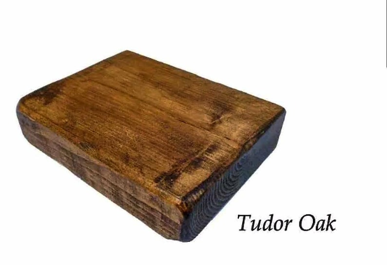 May include: A close-up of a rectangular wooden shelf with a dark brown stain. The shelf has a rough, rustic texture and is labeled "Tudor Oak".