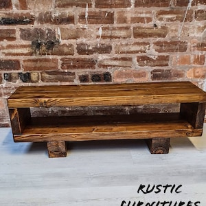 May include: A rustic wooden TV stand with a shelf and four legs. The stand is stained a dark brown color and has a natural wood grain.