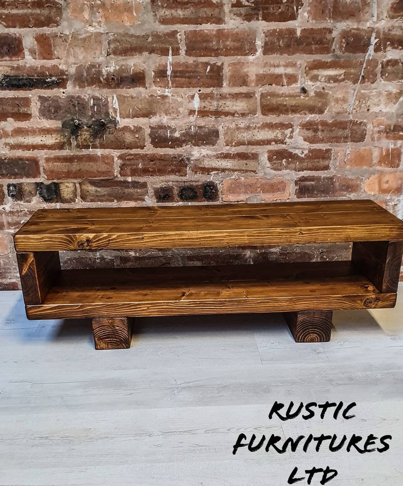May include: A rustic wooden TV stand with a shelf and four legs. The stand is stained a dark brown color and has a natural wood grain.