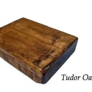 May include: A close-up of a rectangular wooden shelf with a dark brown stain. The shelf has a rough, rustic texture and is made of reclaimed wood. The text "Tudor Oak" is visible below the shelf.