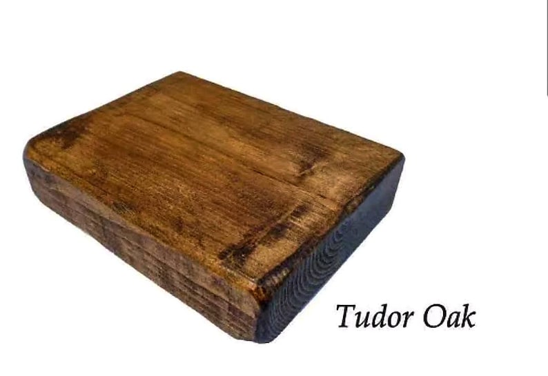 May include: A close-up of a rectangular wooden shelf with a dark brown stain. The shelf has a rough, rustic texture and is made of reclaimed wood. The text "Tudor Oak" is visible below the shelf.