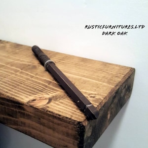 May include: A dark oak wood shelf with a brown metal bracket. The shelf is unfinished and has a rustic look. The text "RUSTICFURNITURES.LTD DARK OAK" is visible on the shelf.
