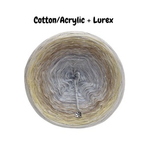May include: A skein of yarn in a gradient of beige, light brown, and silver with a silver lurex thread. The yarn is wound into a ball shape and the label reads "Cotton/Acrylic + Lurex".