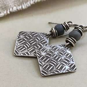 Peut inclure: Boucles d'oreilles en argent avec un charme en métal texturé en forme de diamant et une perle grise sur chaque boucle d'oreille.