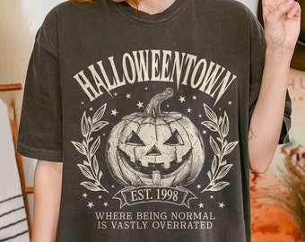 以下が含まれることがあります： 「Halloweentown Est. 1998 Where being normal is vastly overrated」というテキストと、ヴィンテージスタイルのジャック・オー・ランタンのグラフィックが描かれた黒いTシャツです。