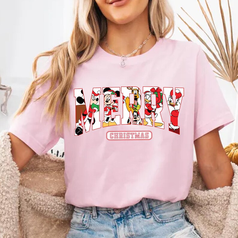 May include: Pink t-shirt with a graphic print of Mickey Mouse and friends spelling out "Merry Christmas".