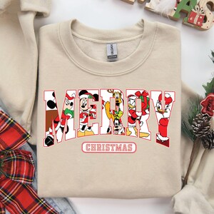 May include: A beige sweatshirt with a red and white "Merry Christmas" graphic featuring Mickey Mouse, Minnie Mouse, Donald Duck, Goofy, and Pluto.
