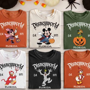 May include: Six t-shirts featuring Disney characters in Halloween costumes. The shirts are in shades of orange, white, and black. Each shirt displays the text "Disneyworld Est. 1971 FLORIDA" in a dripping font, with characters such as Mickey and Minnie Mouse.