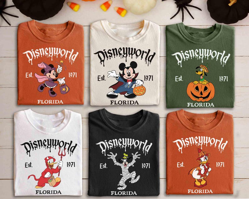 May include: Six t-shirts featuring Disney characters in Halloween costumes. The shirts are in shades of orange, white, and black. Each shirt displays the text "Disneyworld Est. 1971 FLORIDA" in a dripping font, with characters such as Mickey and Minnie Mouse.