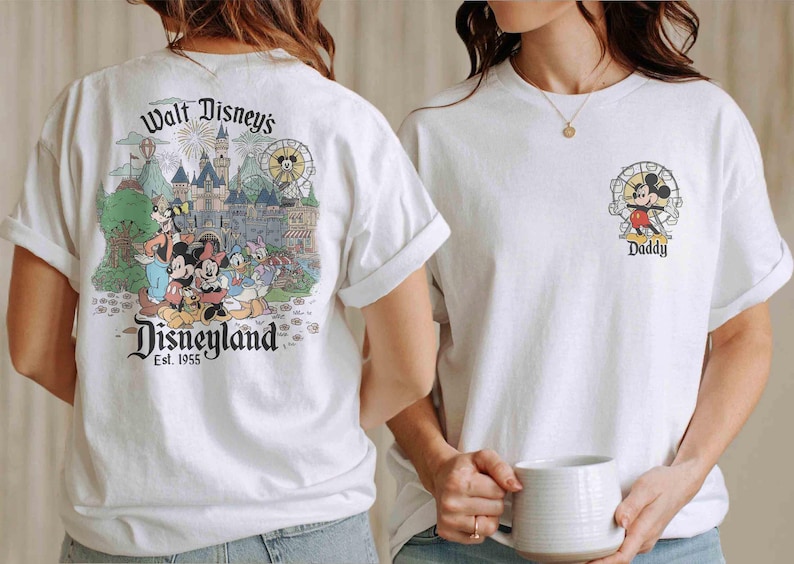 May include: White t-shirts featuring Disney characters. One shirt has a Disneyland graphic on the back, with Mickey, Minnie, Donald, and Goofy. The other shirt has a small Mickey Mouse graphic with the word "Daddy".