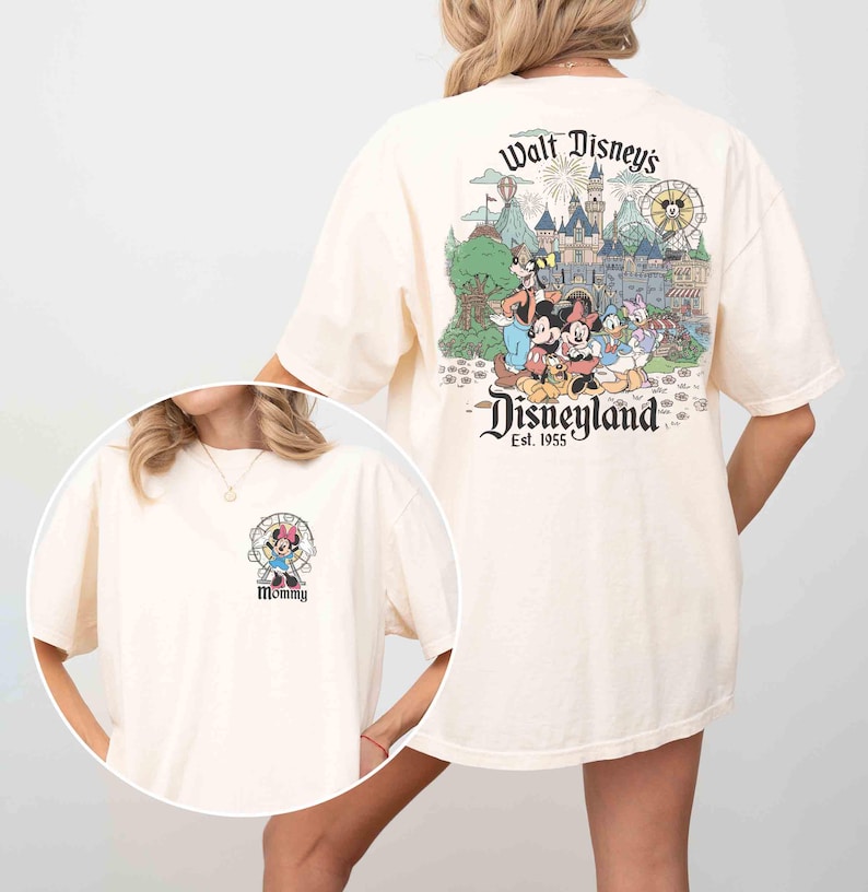 May include: Cream-colored t-shirt featuring a Disneyland graphic on the back with Mickey Mouse, Minnie Mouse, and other Disney characters. The front of the shirt has a small graphic of Minnie Mouse with the word "Mommy".