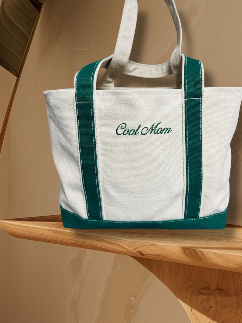 May include: A white canvas tote bag with green trim and the words "Cool Mom" embroidered in green.